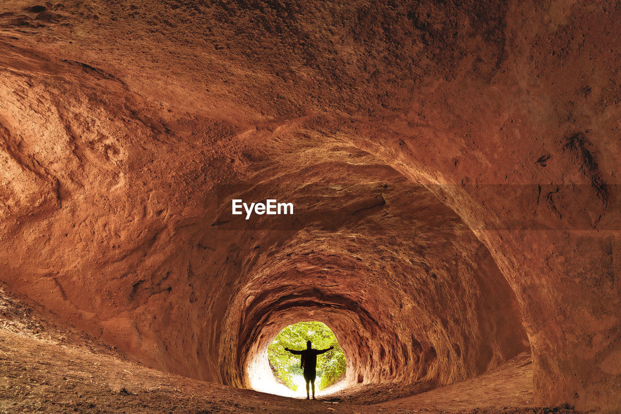 Full frame shot of rock formation in tunnel with a man standing in the entrance.