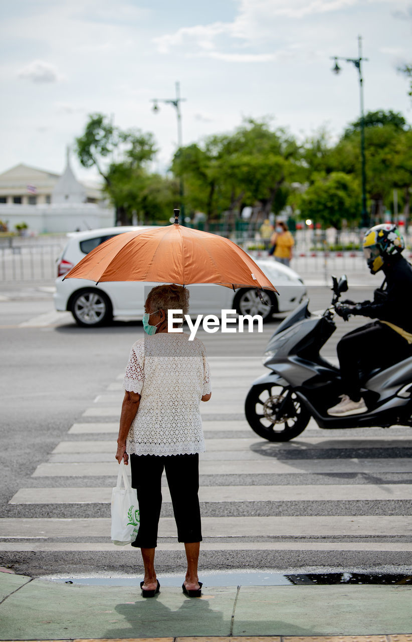 REAR VIEW OF WOMAN WITH UMBRELLA WALKING ON ROAD