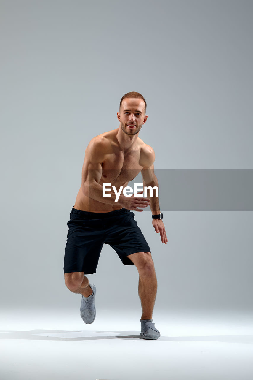 portrait of shirtless young man exercising against white background