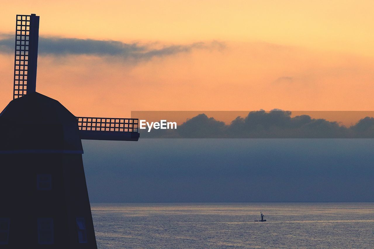 Silhouette traditional windmill by sea against sky during sunset