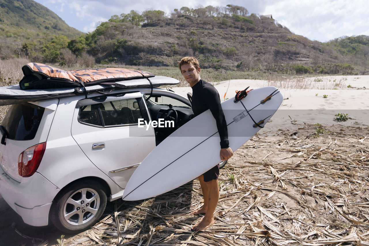 Young man with surfboard near car
