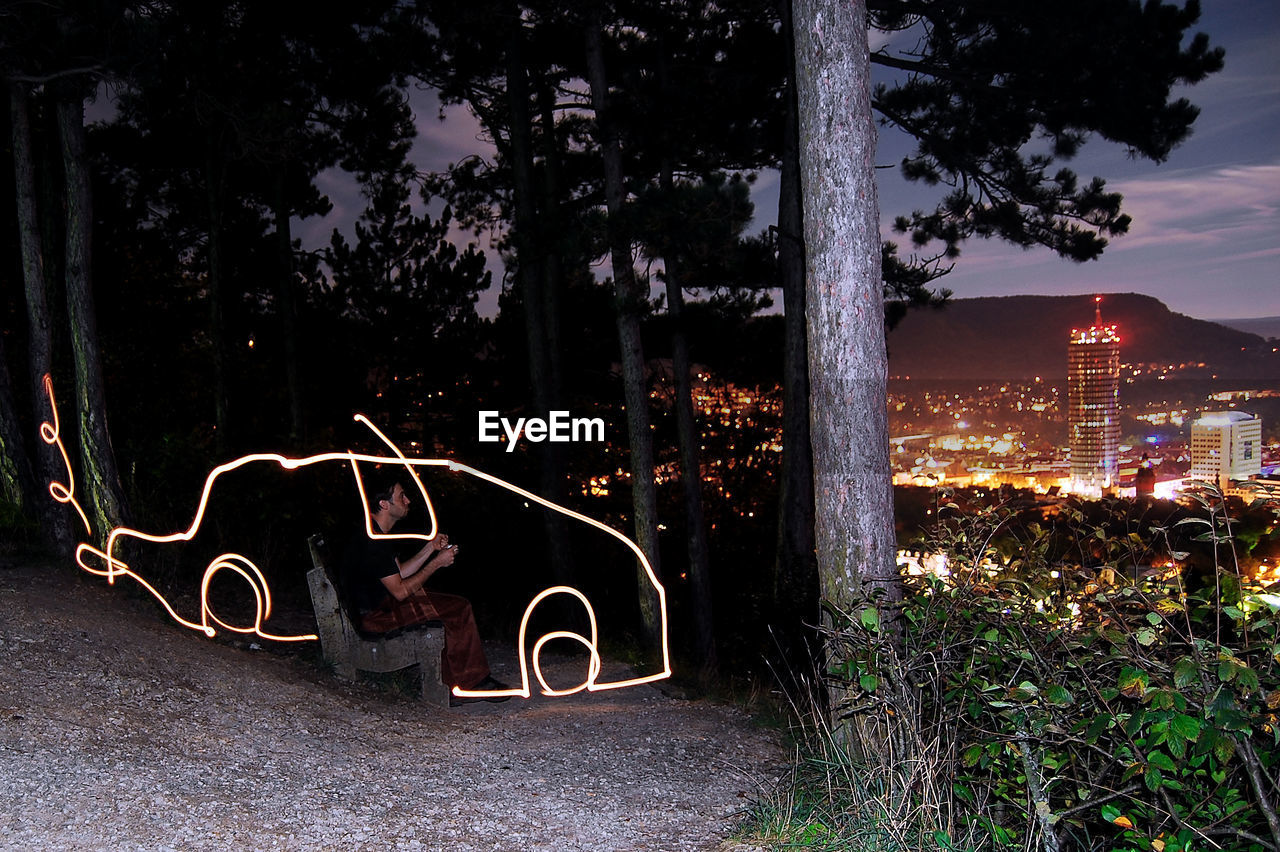 Man driving car created by light painting with illuminated cityscape in background