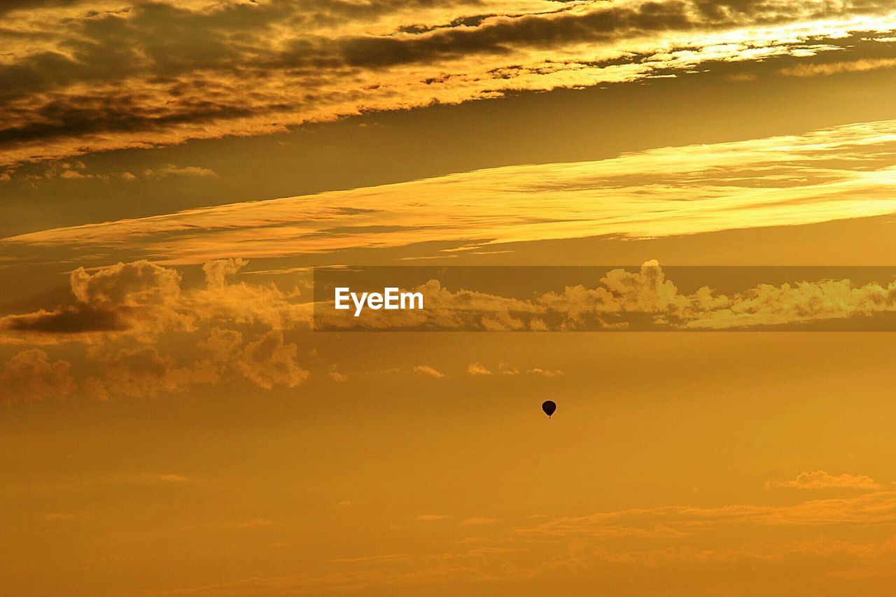Distant view of silhouette hot air balloon against cloudy sky during sunset