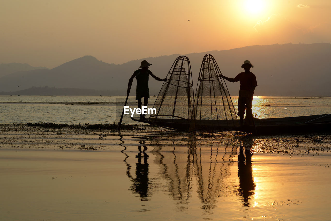 Fishermen fishing in lake with conical fishing nets during sunset