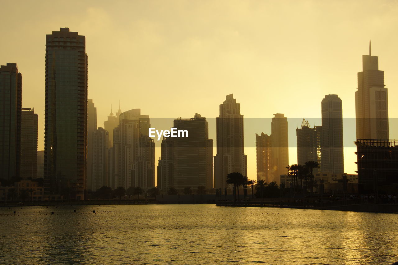 Sea by cityscape against sky during sunset