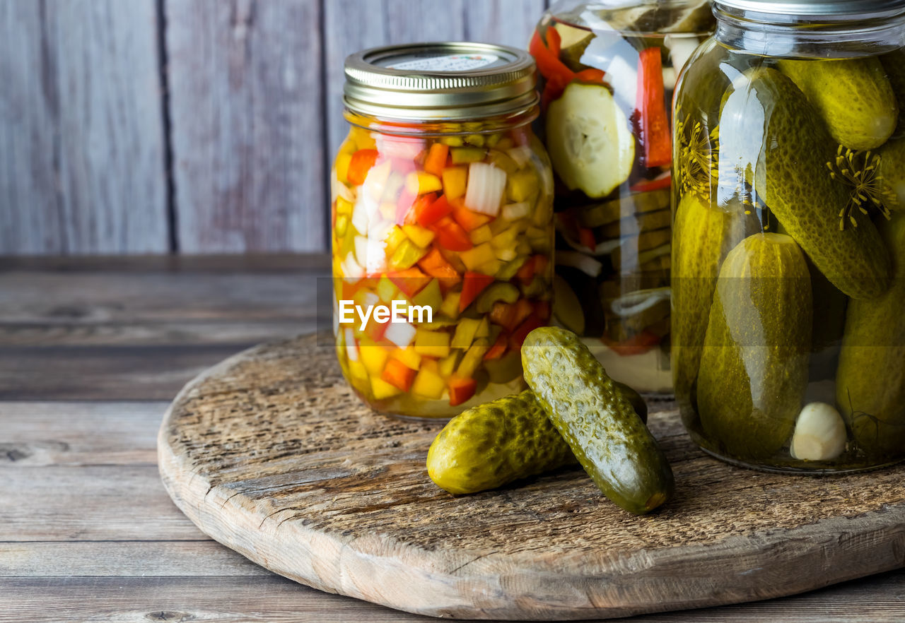 Jars of pickles and peppers against a wooden background.