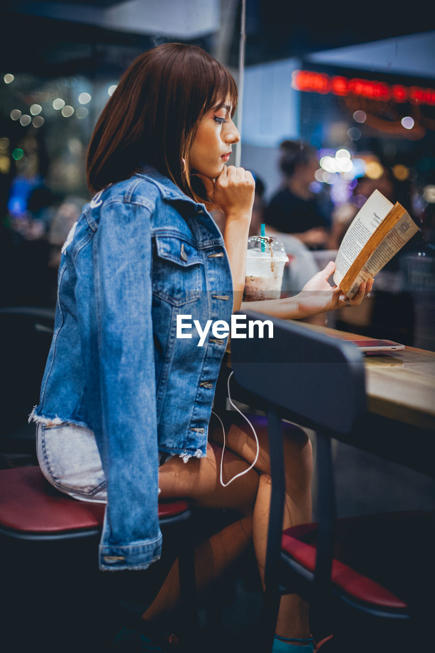 Side view of young woman reading book on restaurant table