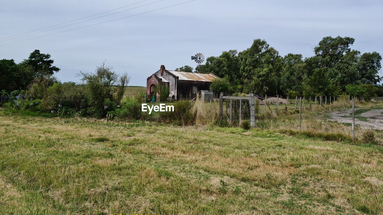 House on field by trees against sky