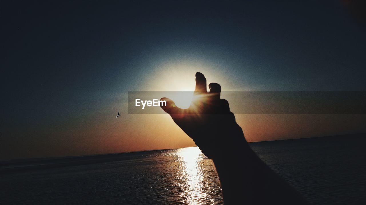 Silhouette hand reaching for sun at beach