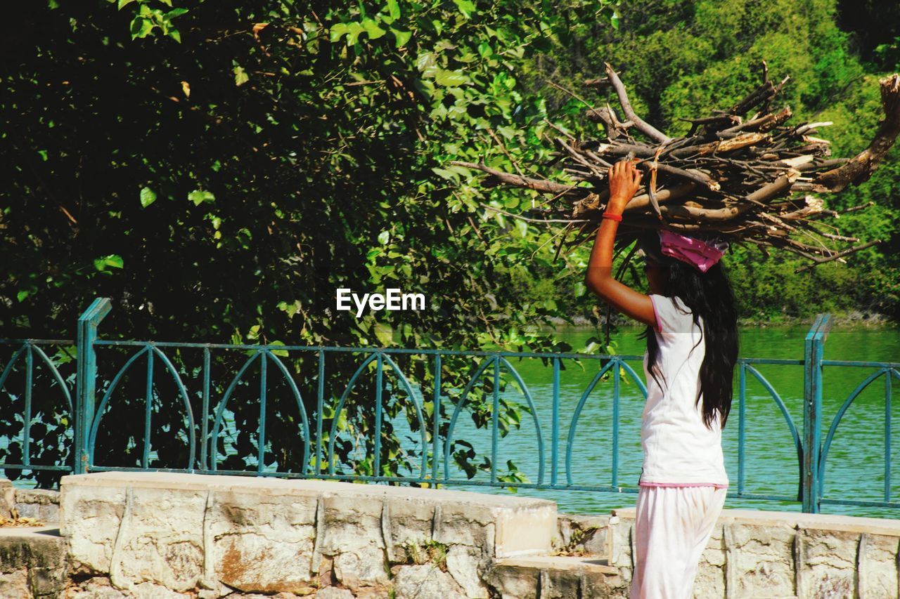 YOUNG WOMAN STANDING BY RAILING AGAINST TREES