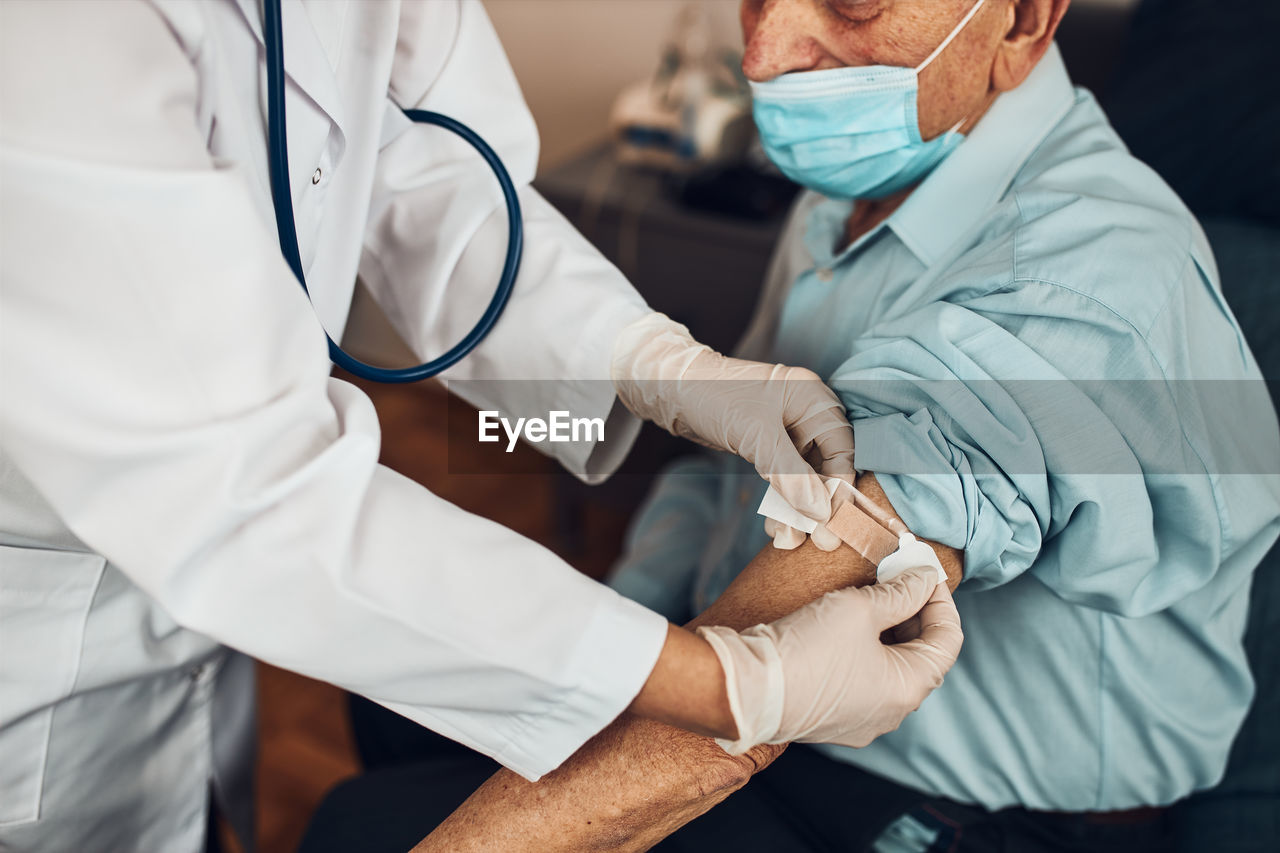 Doctor putting a plaster in place of injection of vaccine to senior man patient. covid-19