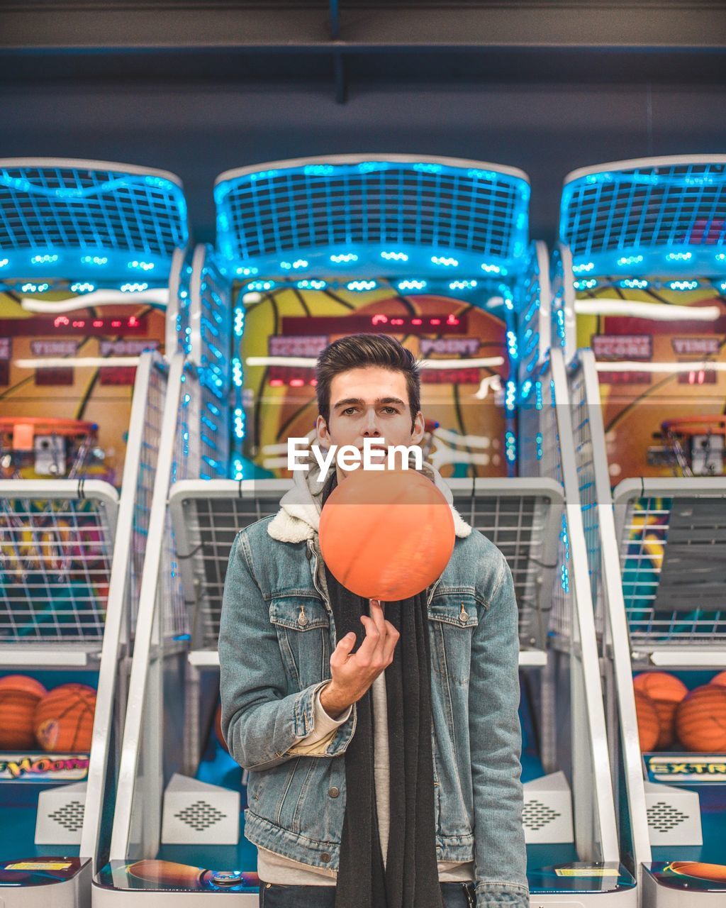 Portrait of young man spinning basketball against amusement arcades