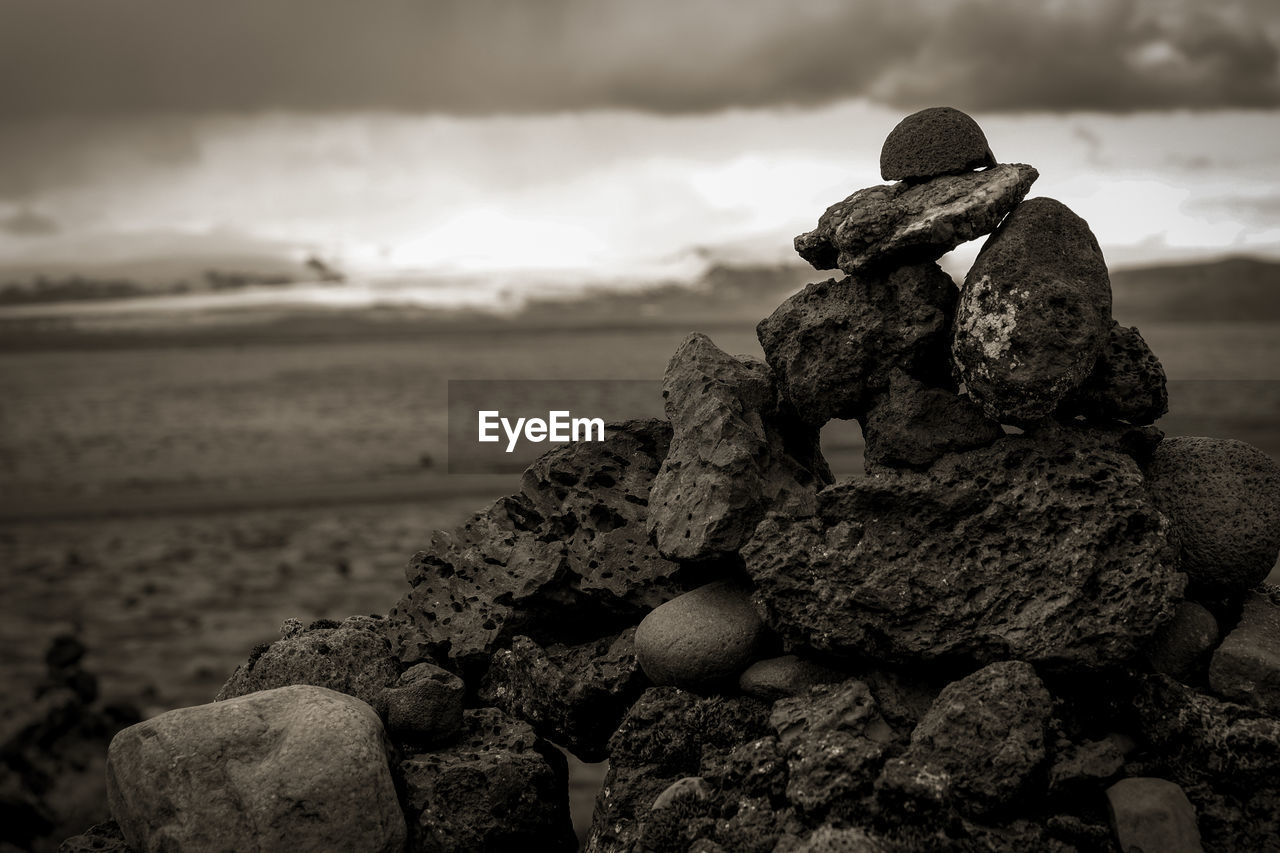 CLOSE-UP OF STONE STACK ON ROCK AT BEACH AGAINST SKY