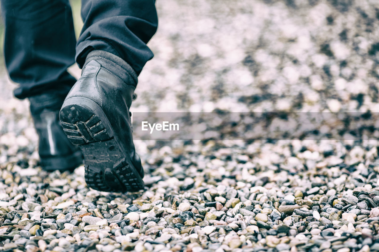 Low section of man walking on pebbles