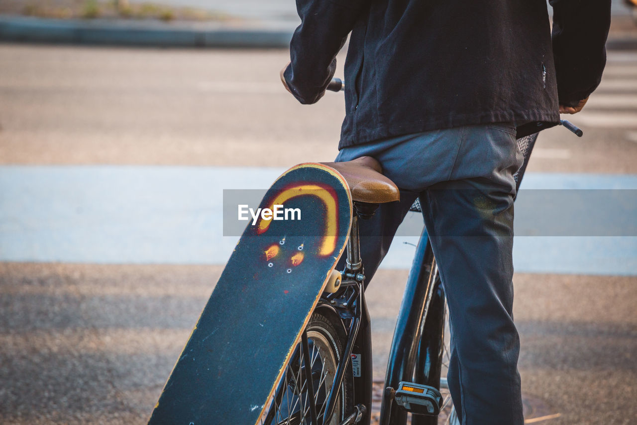 Midsection of man with skateboard on bicycle