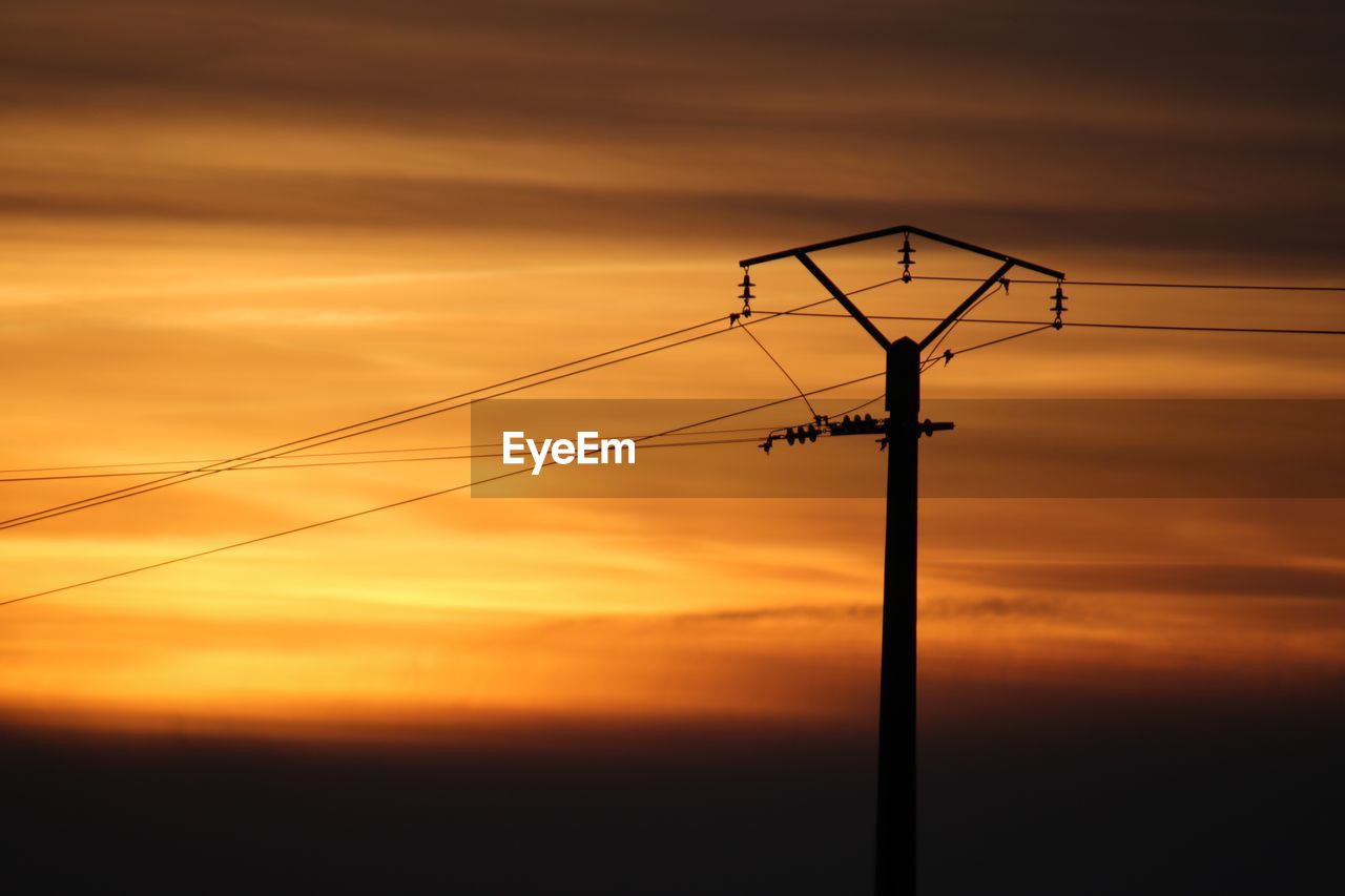 Low angle view of silhouette electricity pylon against dramatic sky during sunset