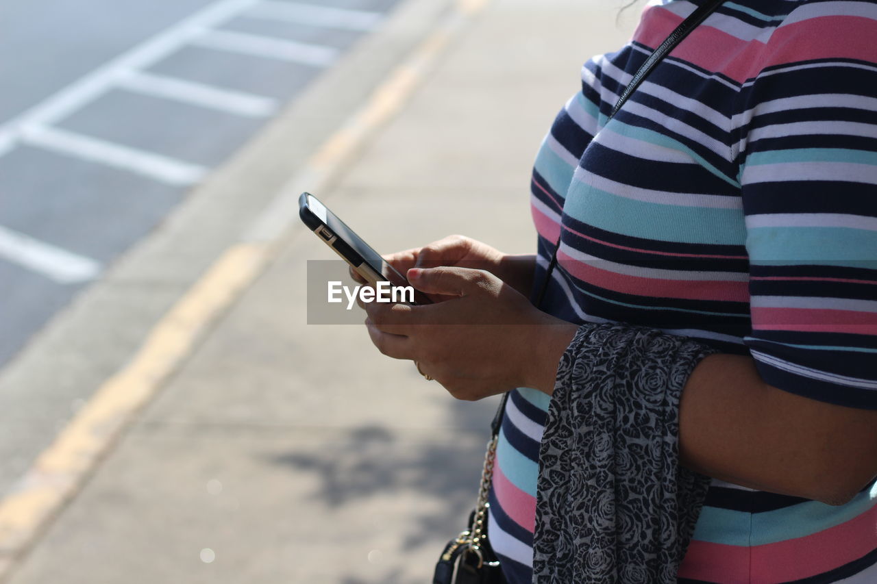 Midsection of woman using mobile phone while standing on sidewalk