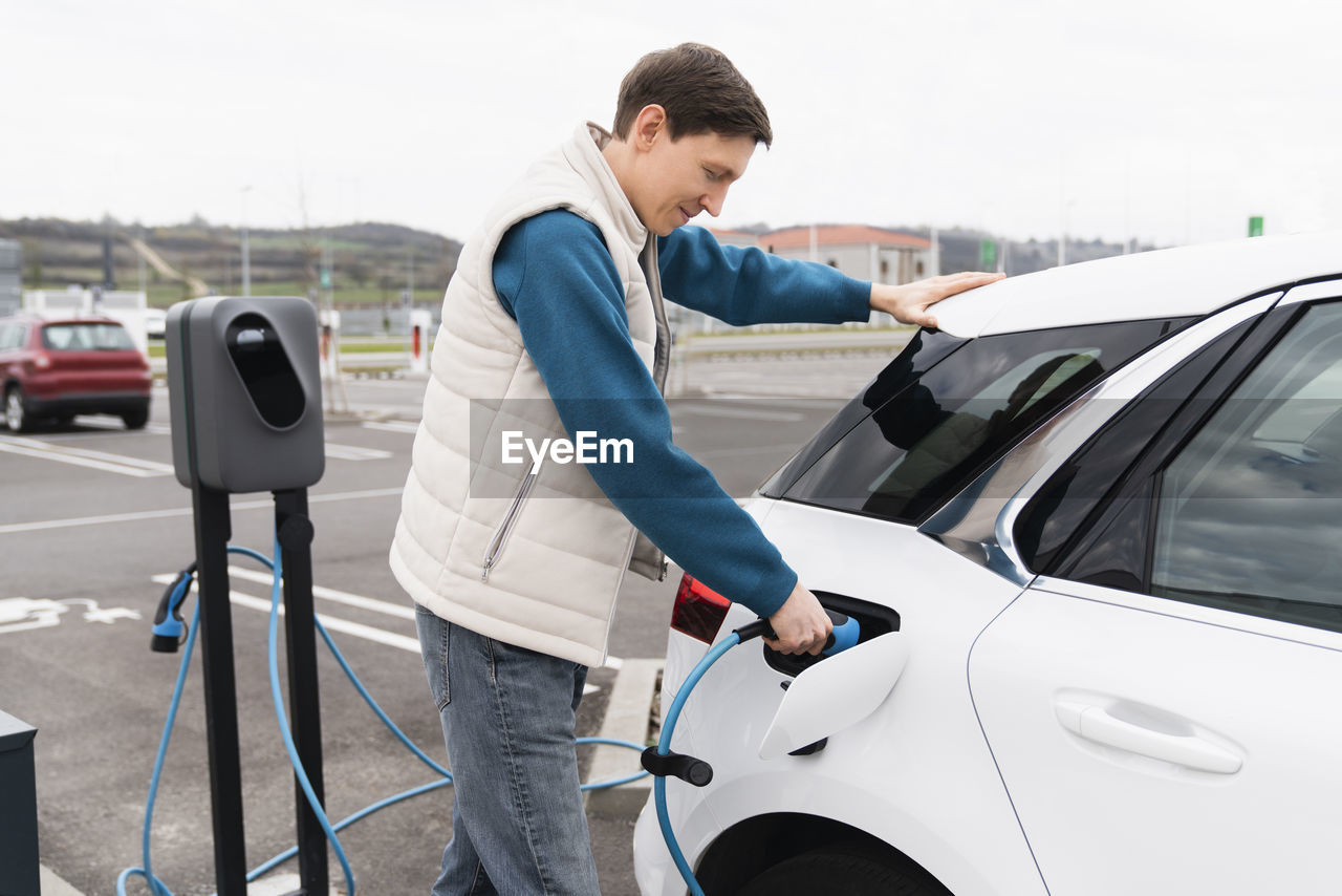 Man plugging charger in electric car at station