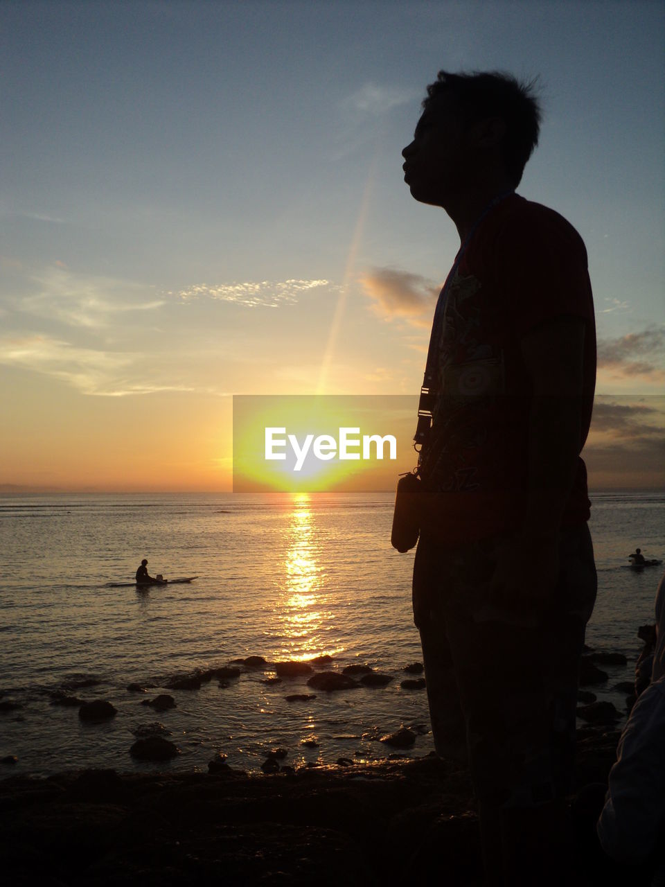 Side view of silhouette man standing at beach against sky during sunset