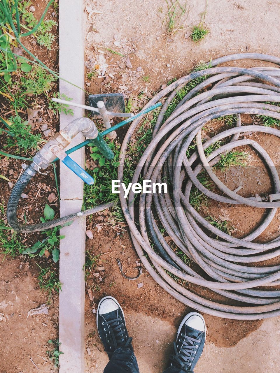 Low section of man standing by garden hose