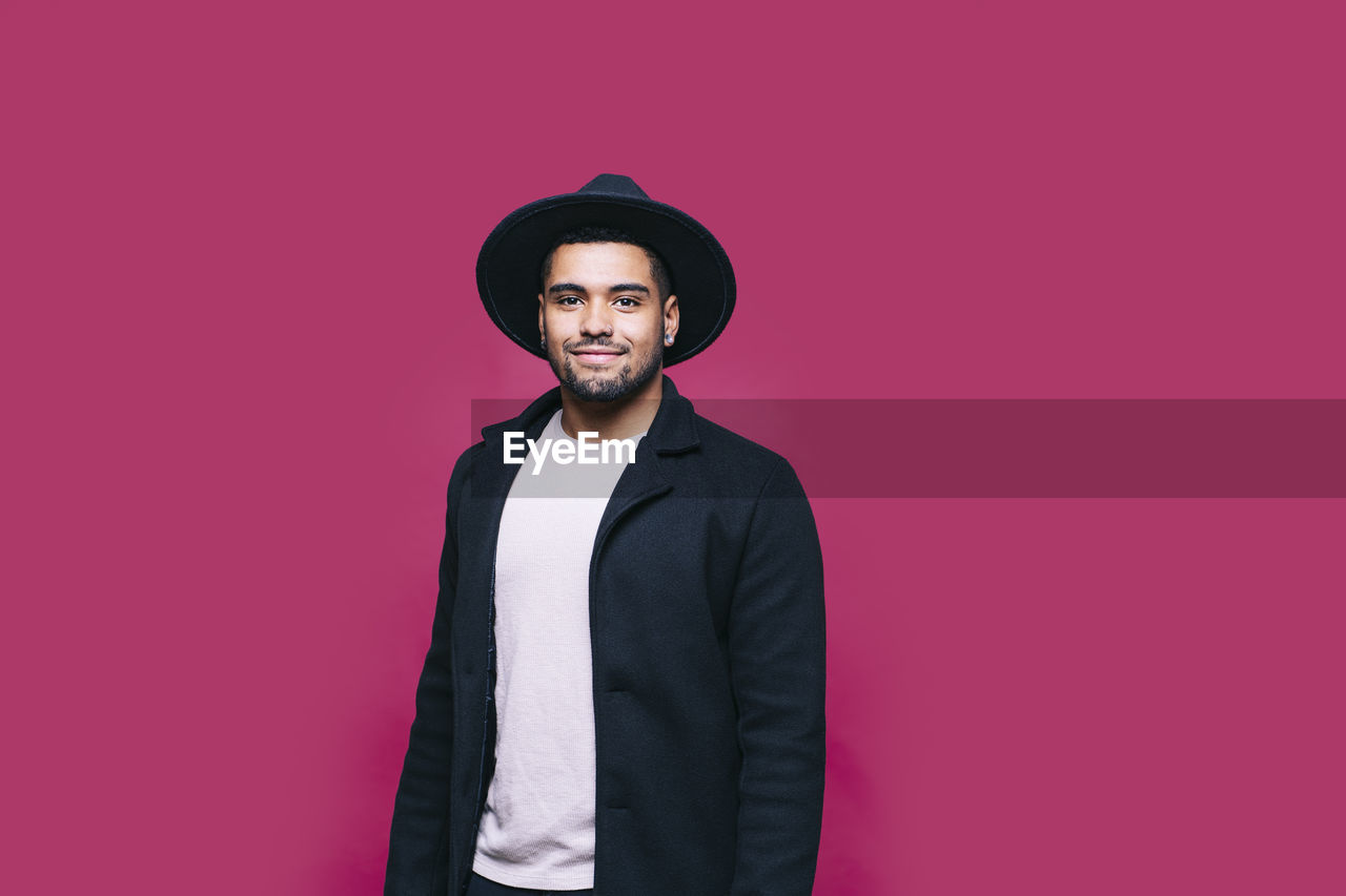 Smiling man in jacket standing against pink background