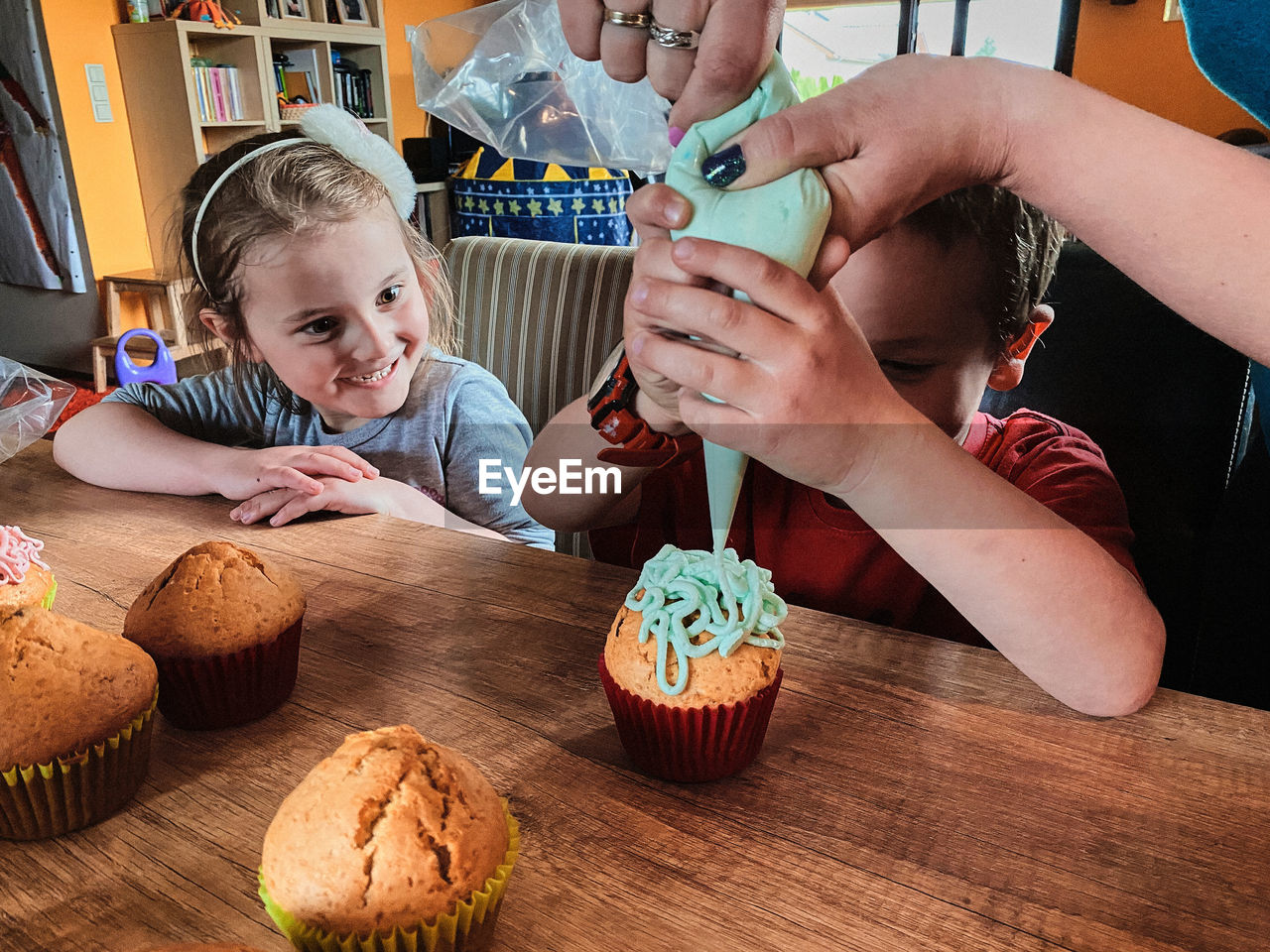 Group of children baking cupcakes, squeezing cream from confectionery bag, preparing ingredients