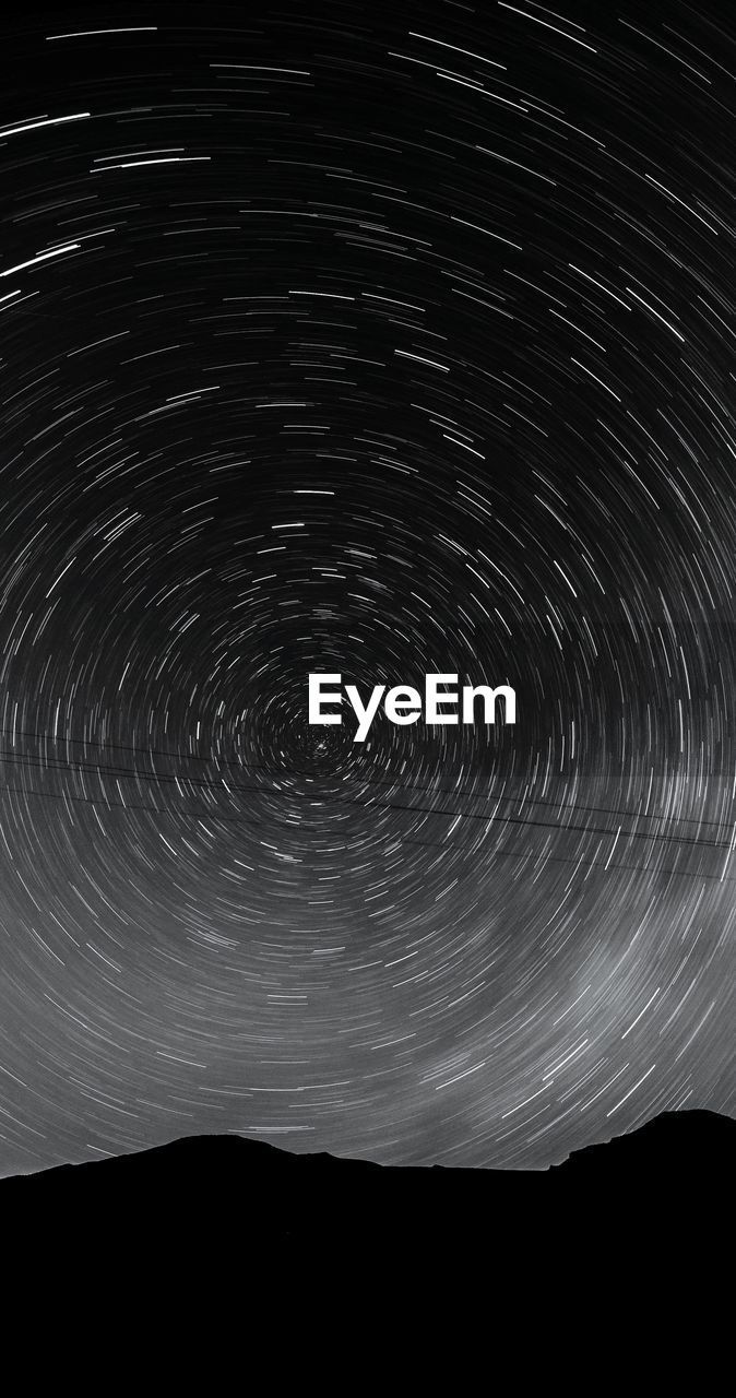 Low angle view of star trails above silhouette mountains at night