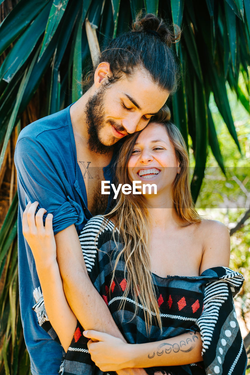 Gentle multiethnic couple standing face to face with closed eyes and enjoying romantic moments in tropical park