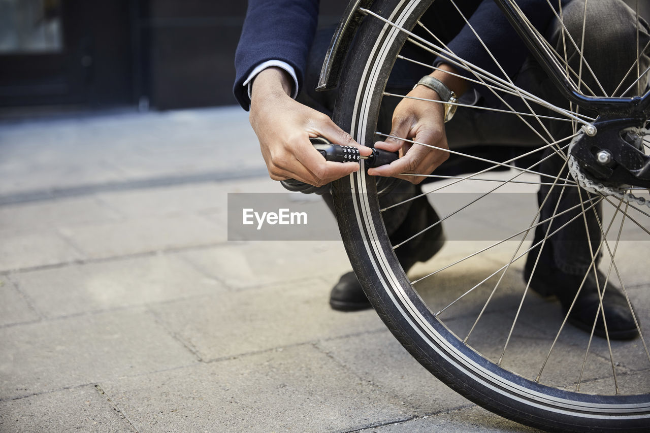 Low section of male commuter locking electric bicycle wheel against building in city