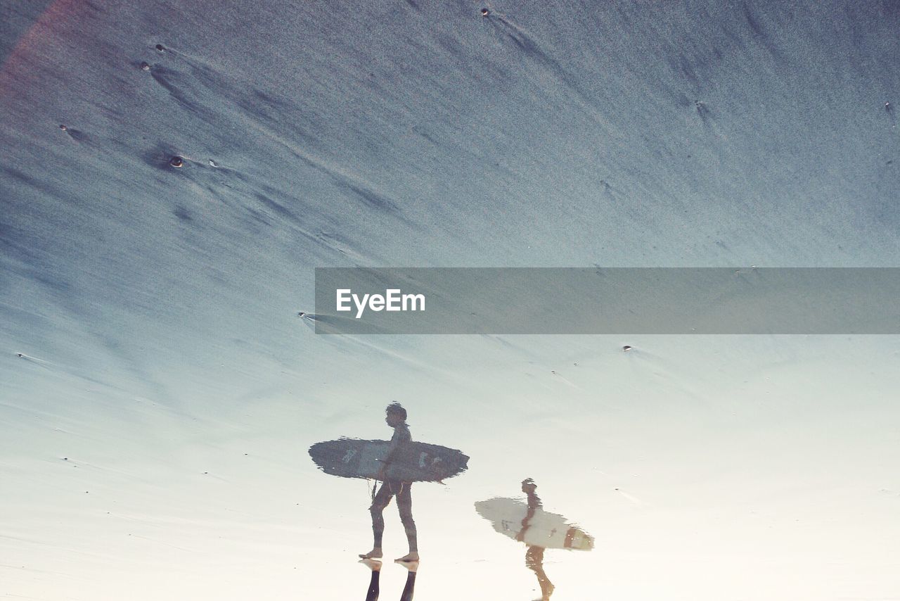 People with surfboard reflected on wet beach