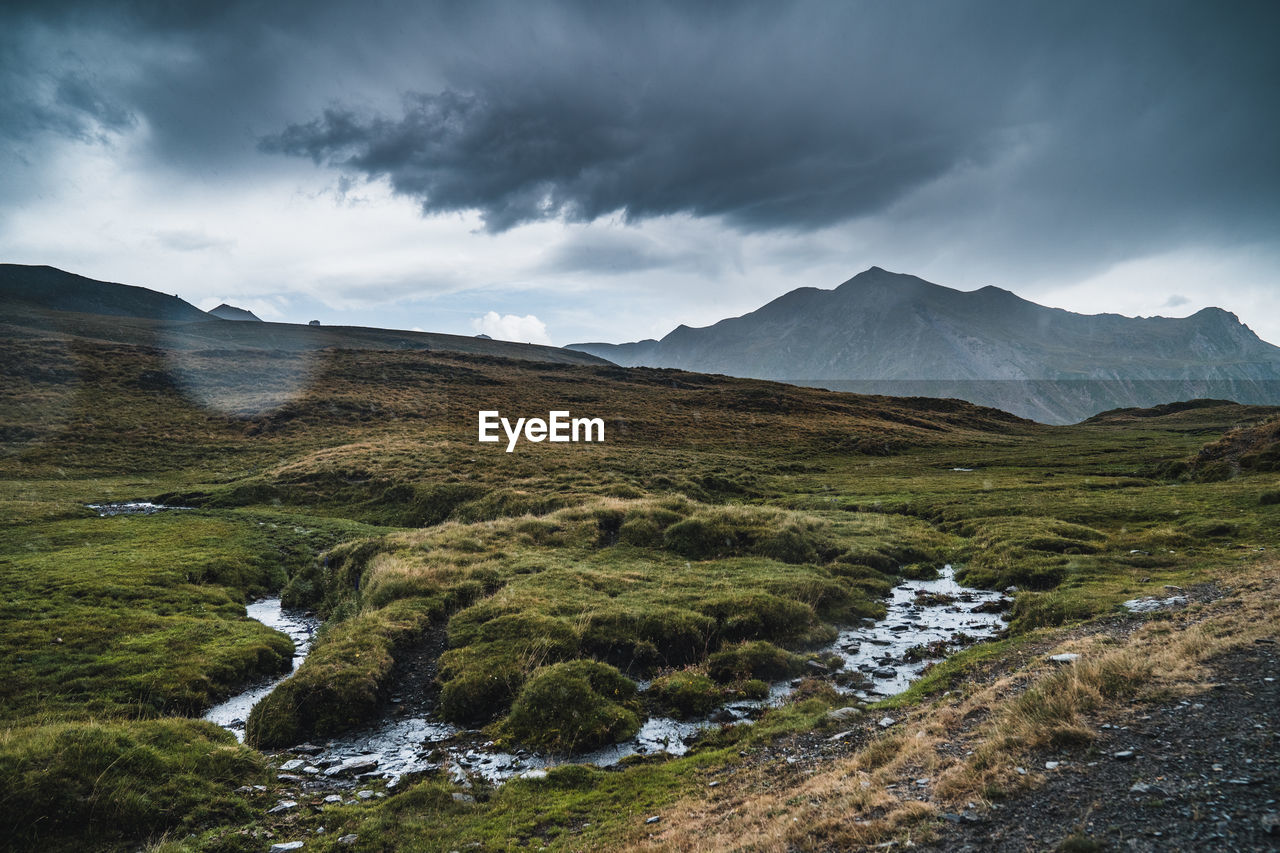 Breathtaking landscape of meadow with green grass and creek flowing on hills under gloomy sky in pyrenees in spain