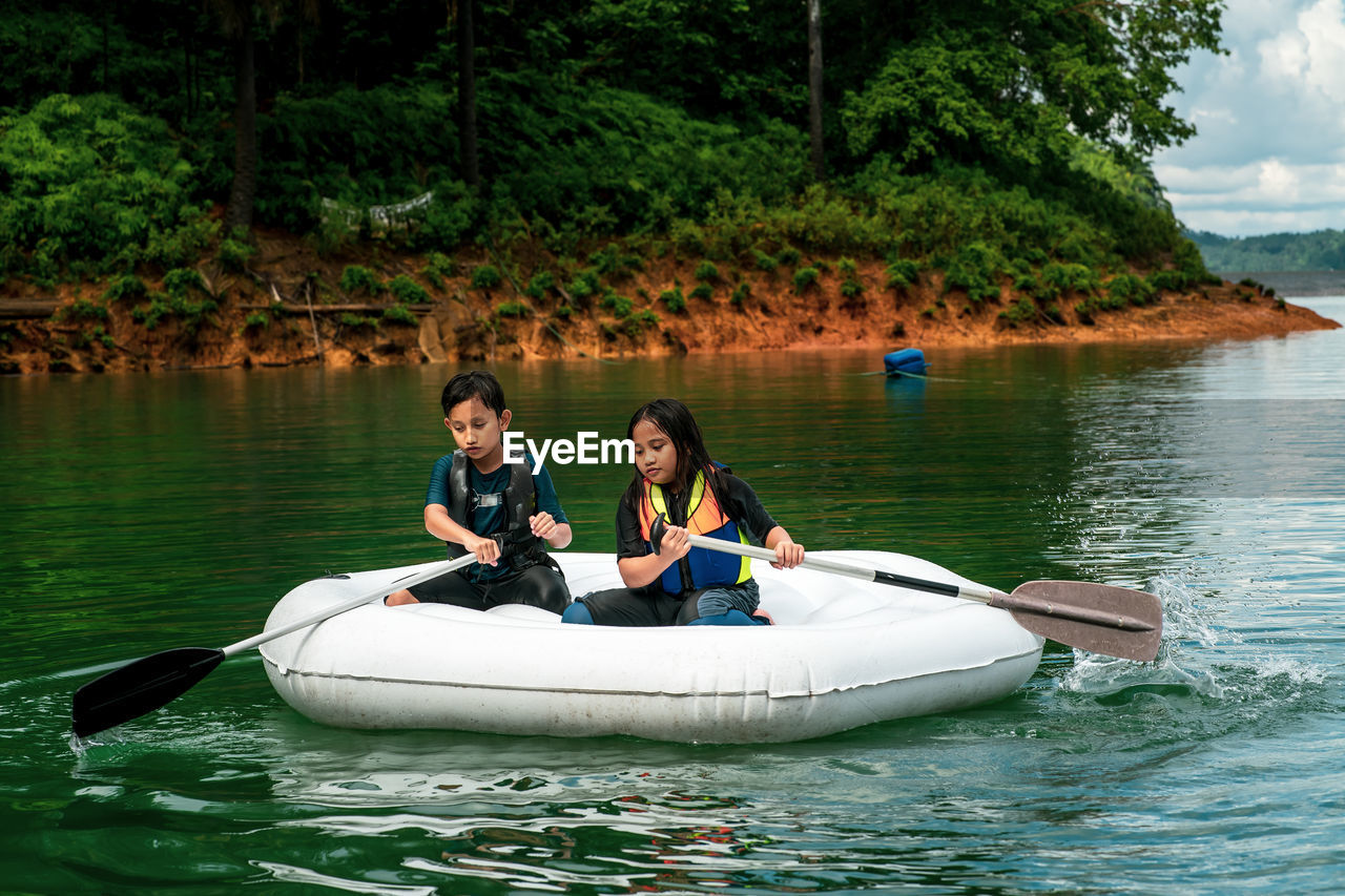 Children wearing life jackets paddling on an inflatable boat in kenyir lake, malaysia.