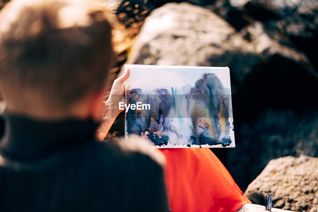 REAR VIEW OF MAN PHOTOGRAPHING ROCK ON ROCKS