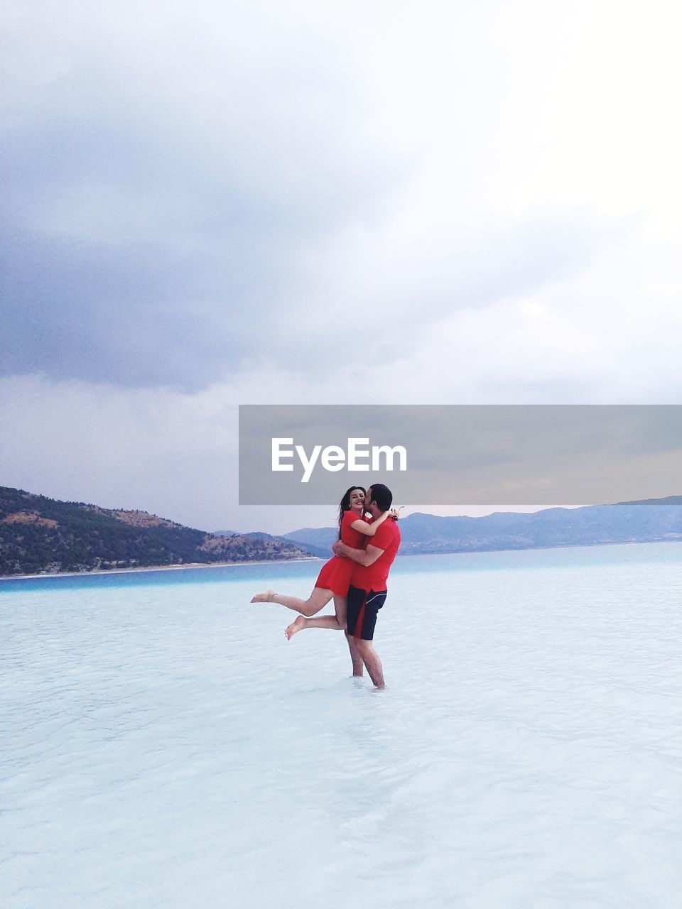 Couple embracing while standing at shore against sky