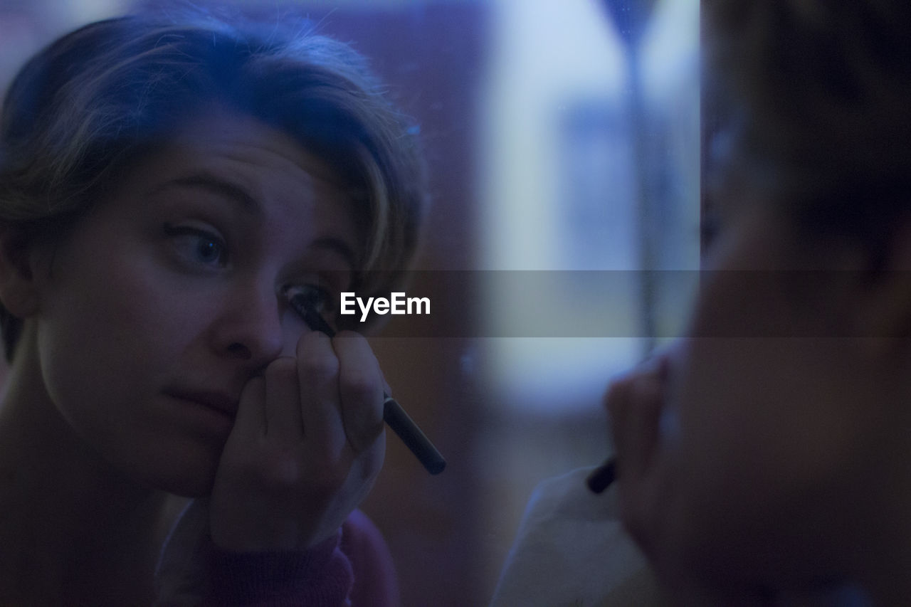 Reflection of young woman applying mascara on mirror