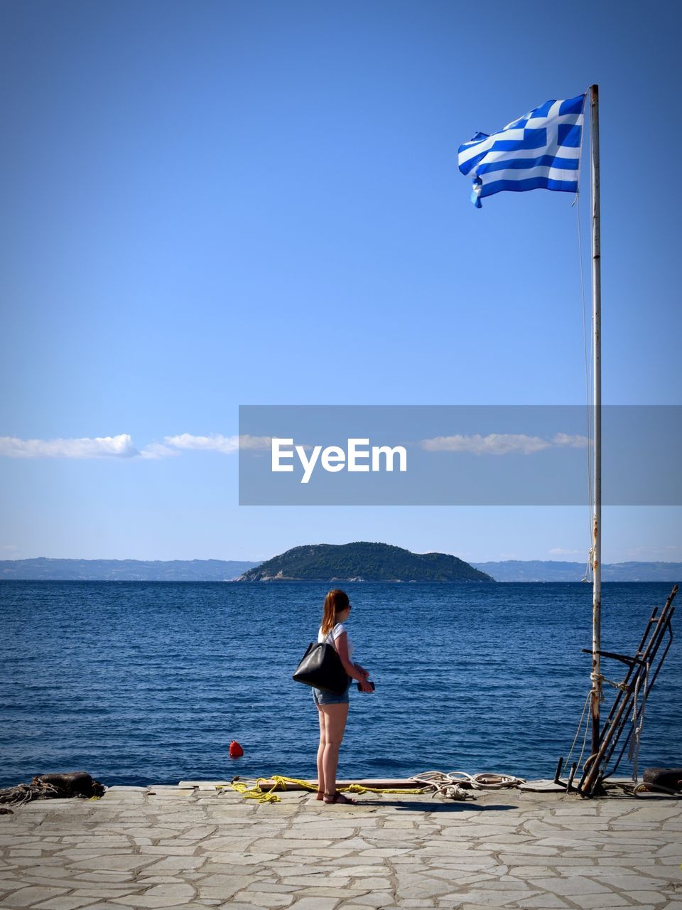 Side view of woman standing by greek flag against sea