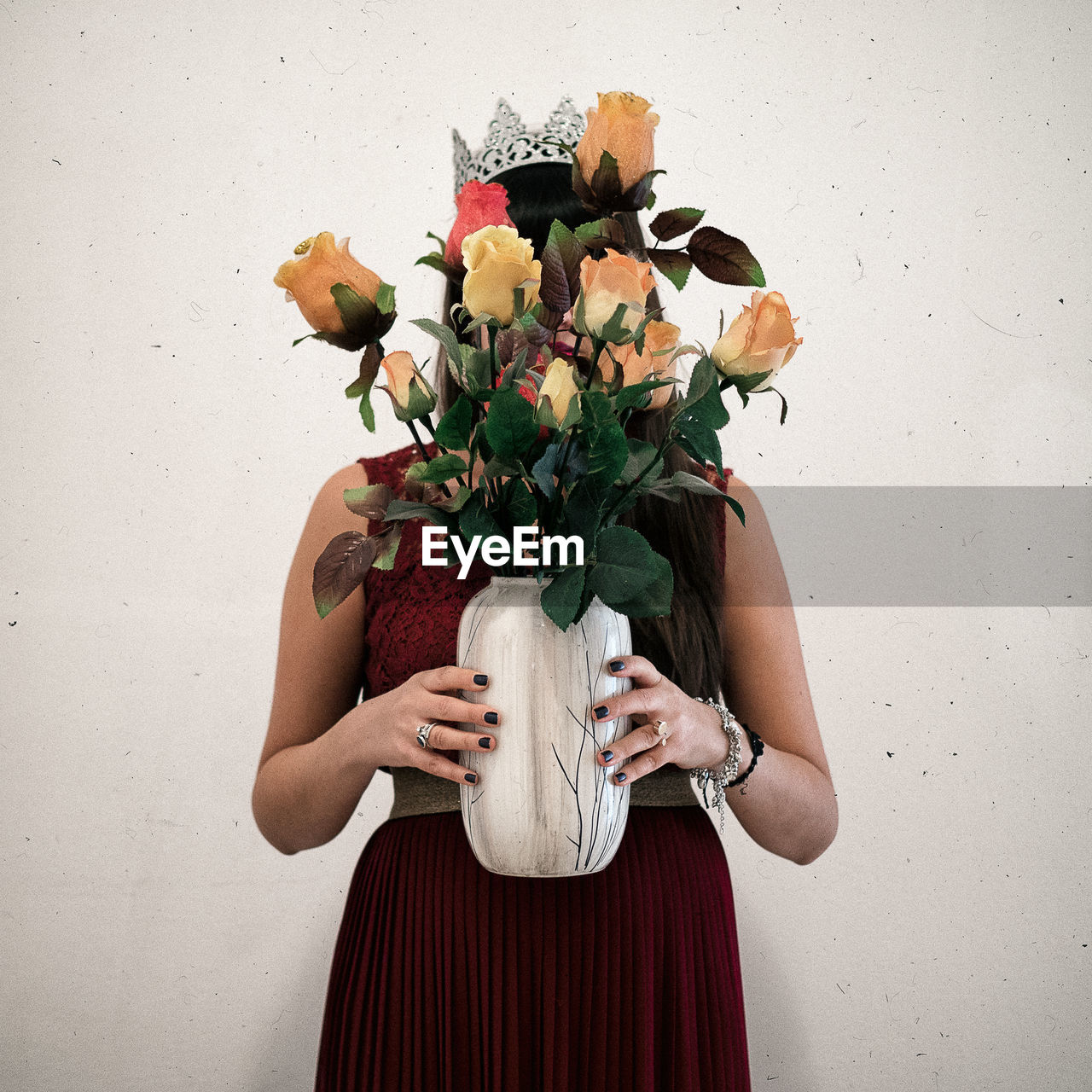 Woman holding flower vase while standing against wall
