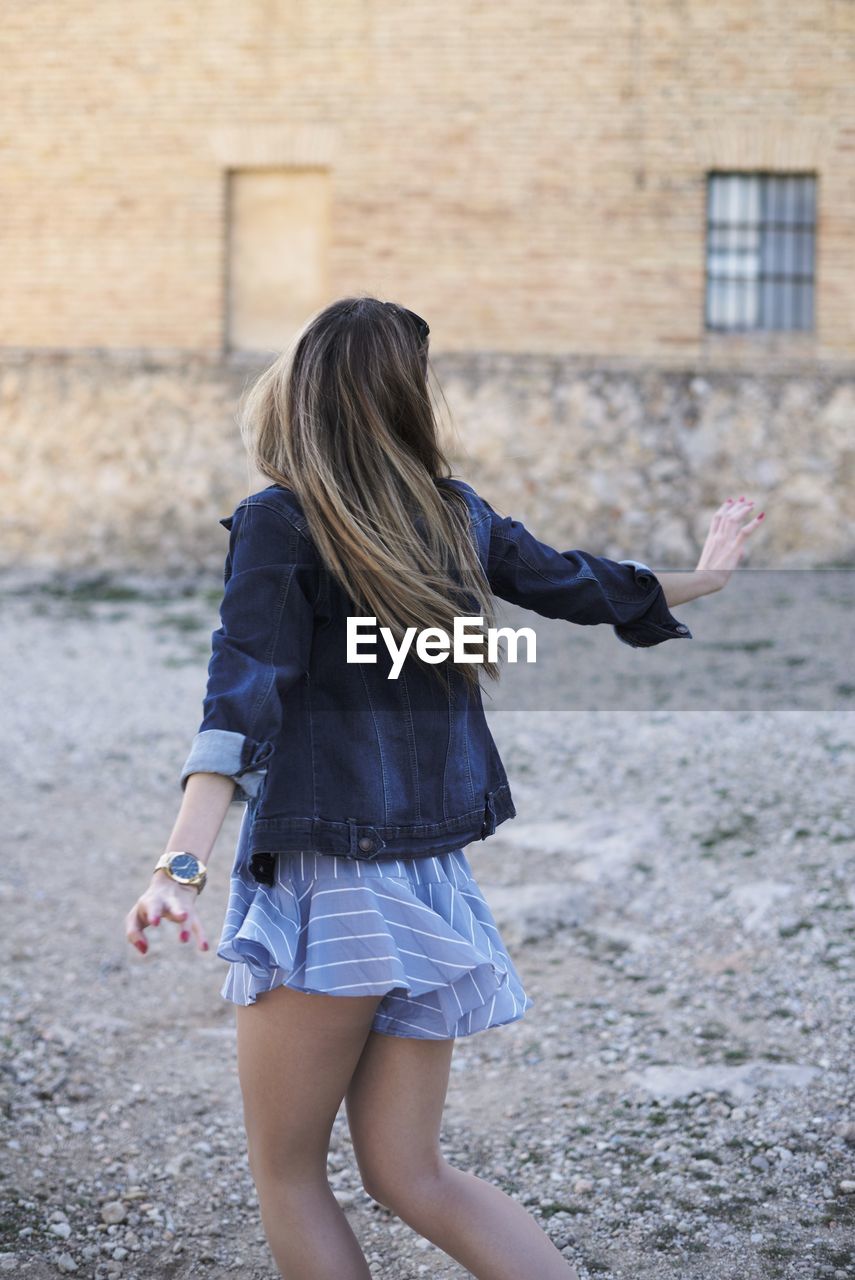 Back view of anonymous young female in trendy outfit turning around with outstretched arms while enjoying freedom in summer