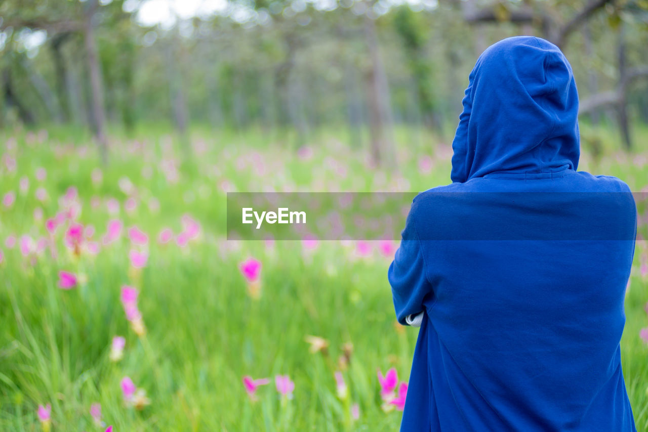 plant, rear view, one person, nature, land, flowering plant, flower, field, blue, meadow, women, adult, clothing, beauty in nature, hood, grassland, lifestyles, growth, landscape, outdoors, standing, waist up, day, green, focus on foreground, three quarter length, environment, hood - clothing, traditional clothing, natural environment, child, purple, freshness