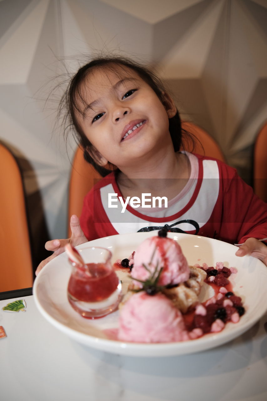 Portrait of a kid with strawberry ice cream in plate