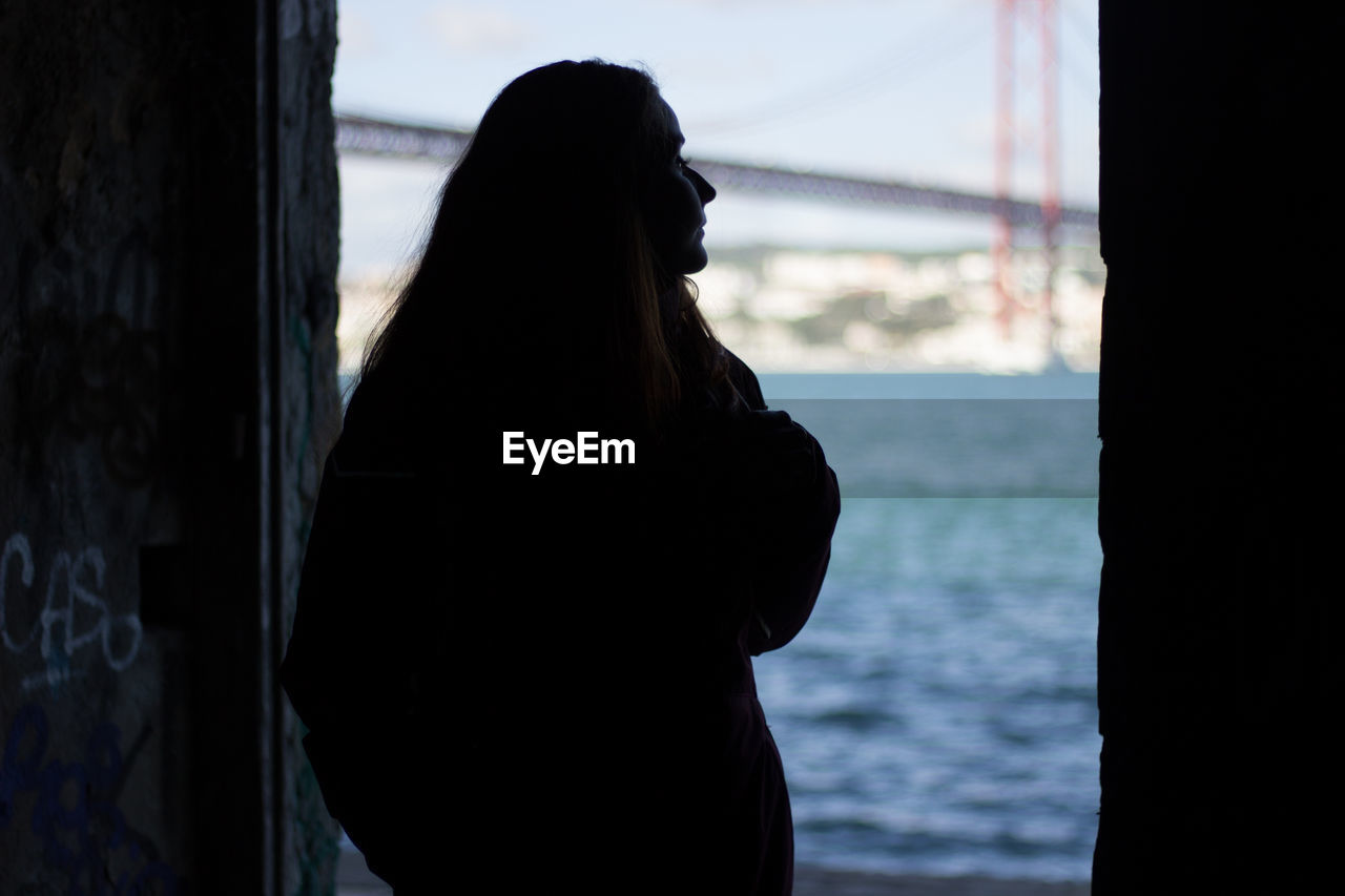 Rear view of silhouette woman standing on doorway by sea