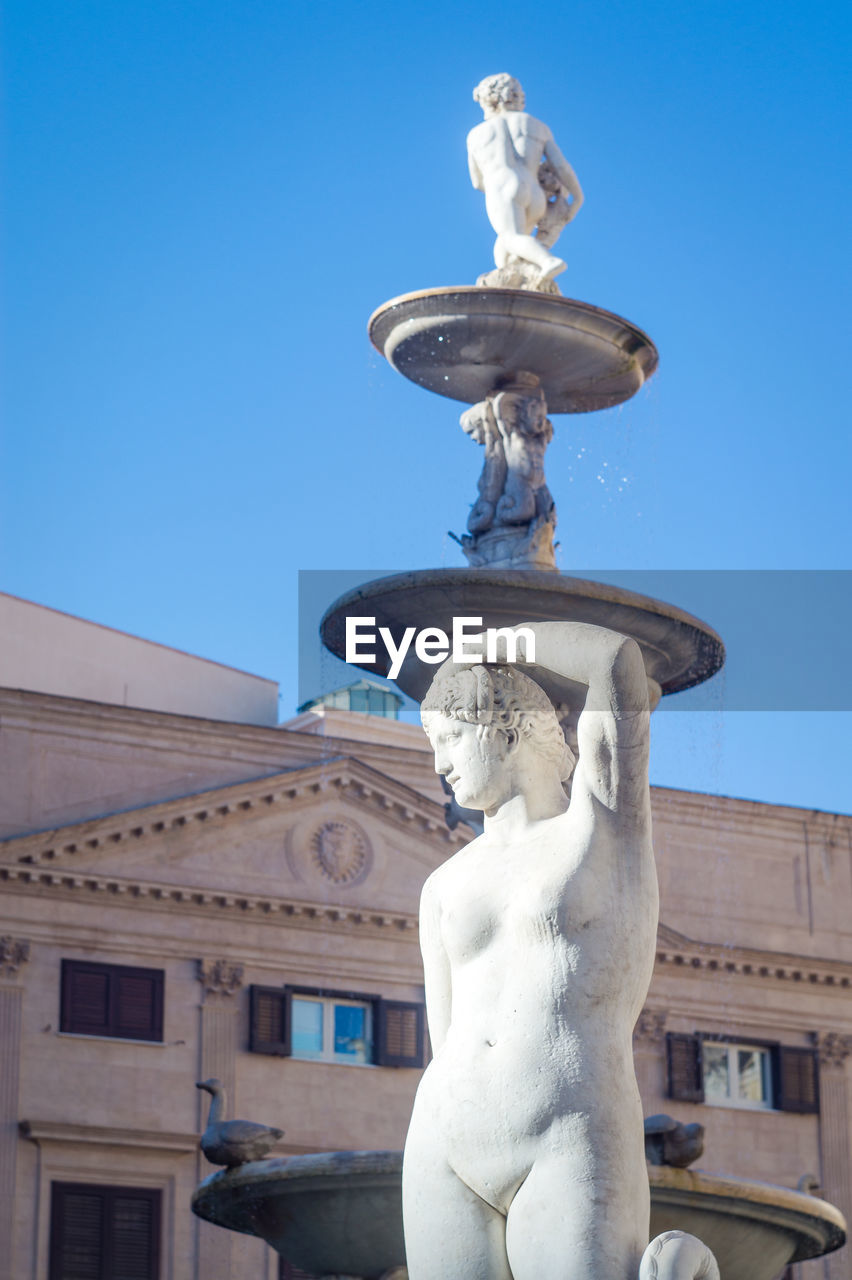 LOW ANGLE VIEW OF STATUE AGAINST BUILDING AGAINST BLUE SKY