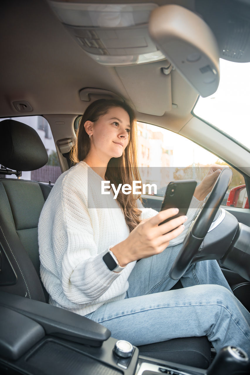 smiling using mobile phone while sitting in car