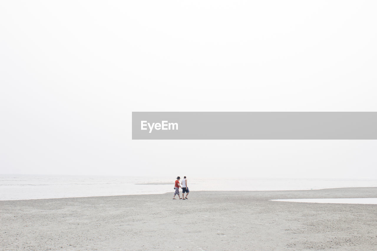 Men walking on beach against clear sky