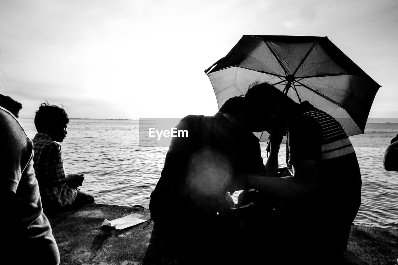 PEOPLE SITTING ON BEACH AGAINST SKY