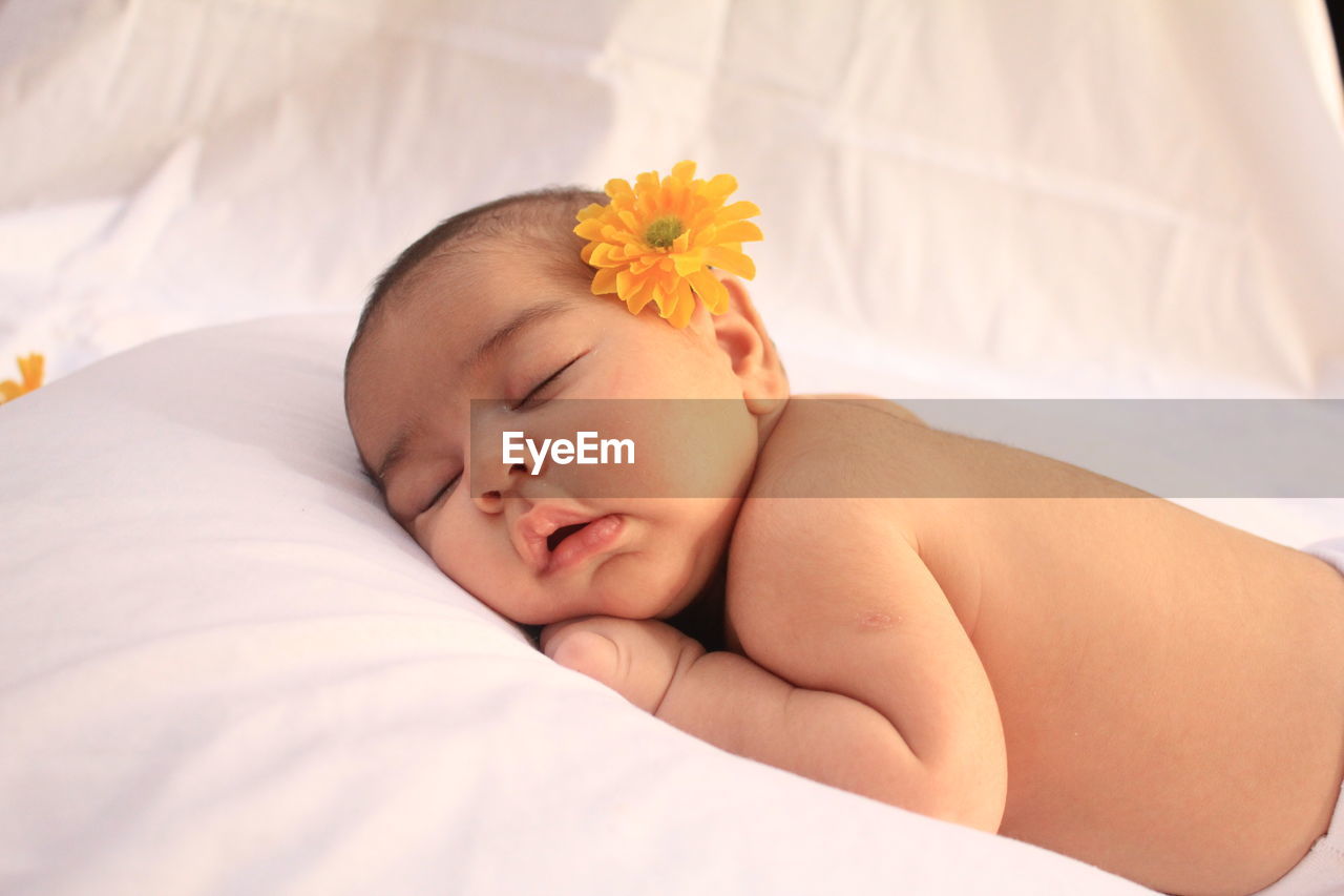 Close-up of baby girl with flowers on bed
