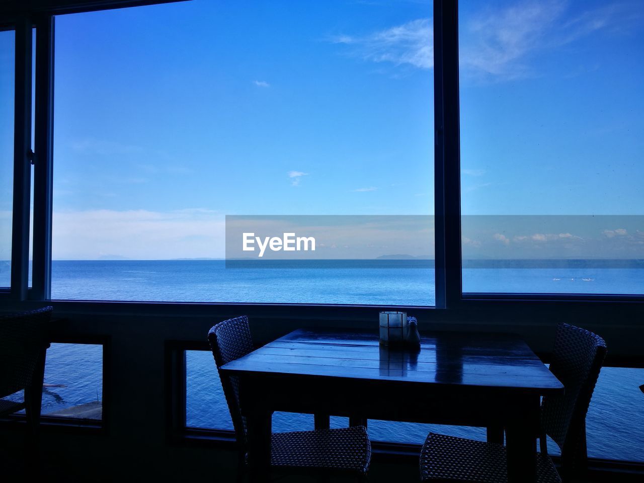 CHAIRS AND TABLE BY SEA AGAINST SKY SEEN FROM WINDOW