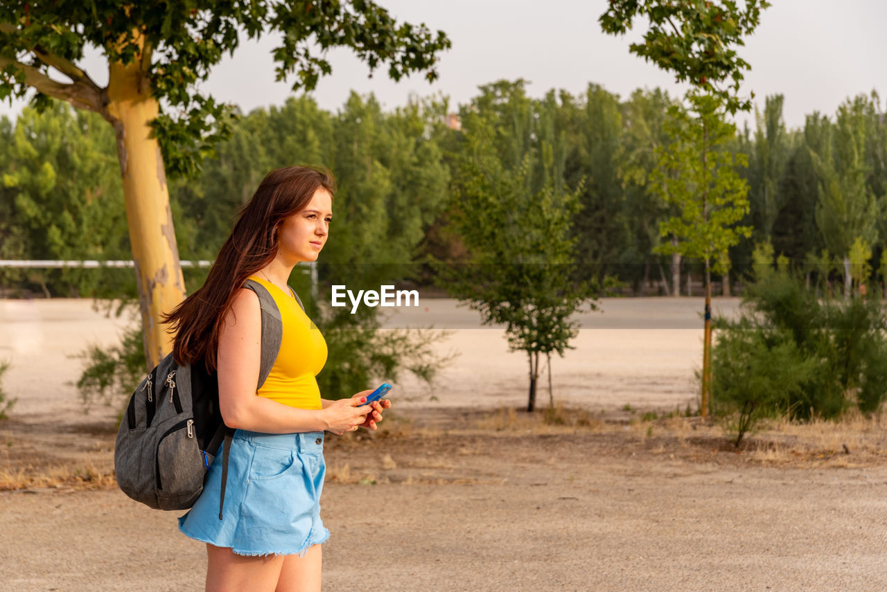 Young caucasian girl walking in the park using mobile phone