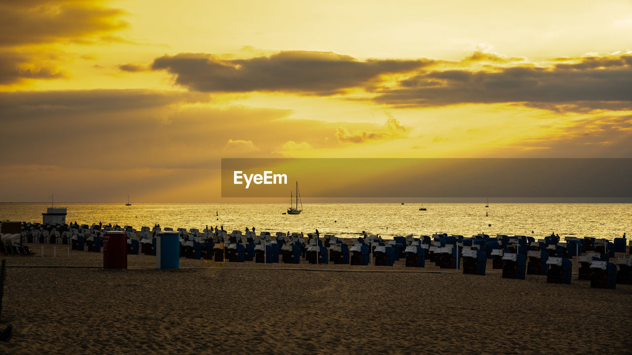 Deck chairs on beach against sky during sunset