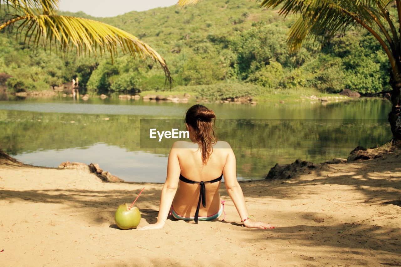 Rear view of woman sitting on beach against sky